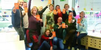 Foto: Genossenschaft für Gemeinwohl Eine Gruppe von Menschen zeigt eine orange Karte her, auf der ein Kugelschreiber im Kreis abgebildet ist Kugelsc
